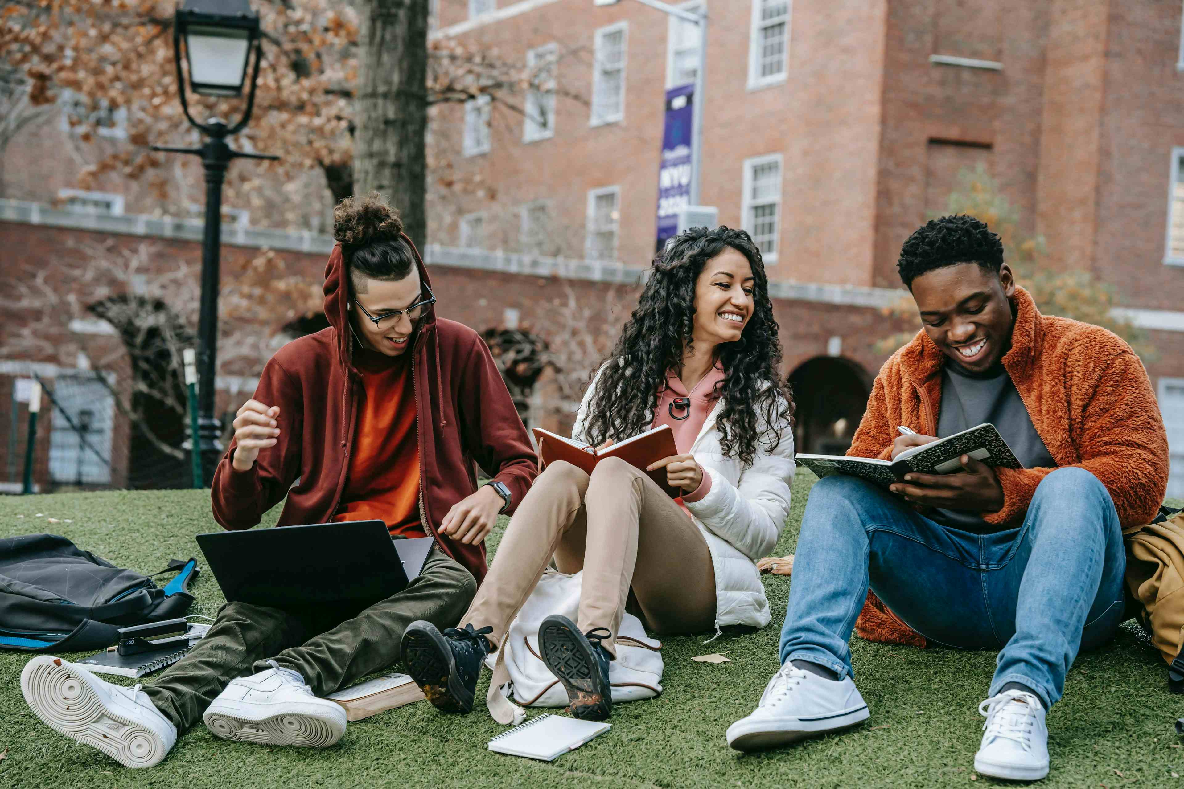 Three students sitting on the grass at a college campus